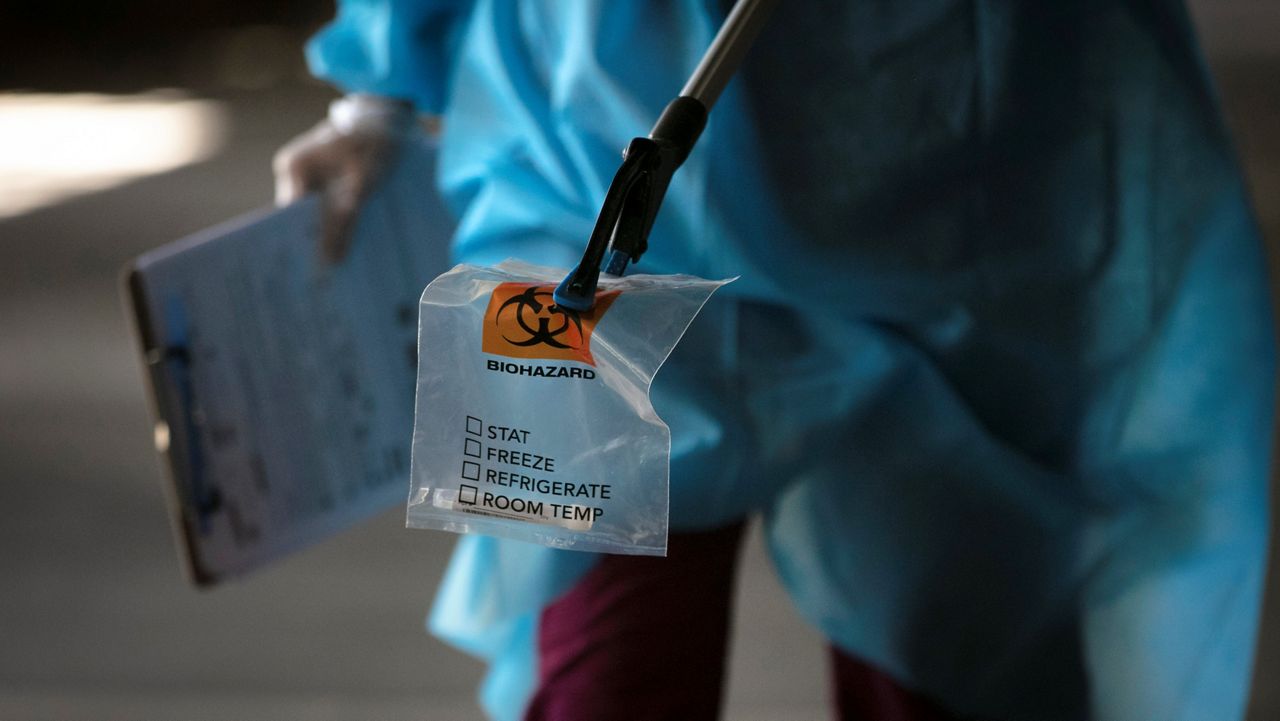A physician assistant carries a nasal swab sample using a grabber at a COVID-19 drive-through testing site set up at the Anaheim Convention Center in Anaheim, Calif., Thursday, July 16, 2020. Rising coronavirus infections across dozens of states are threatening the U.S. economic recovery, forcing businesses and consumers to freeze spending and keeping the unemployment rate stubbornly high. (AP Photo/Jae C. Hong)