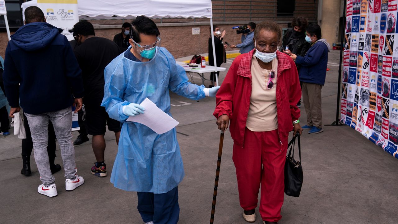 Vera Eskridge, right, is escorted into the waiting area by registered nurse Angelo Bautista after getting her COVID-19 vaccine at a vaccination site in the parking lot of the Los Angeles Mission in the Skid Row area of L.A., Feb. 10, 2021. (AP/Jae C. Hong)