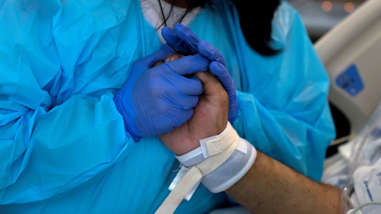 In this February 15, 2021, file photo, Patty Trejo, 54, holds the hand of her intubated husband, Joseph, in a COVID-19 unit at St. Jude Medical Center in Fullerton. Trejo visited her husband Monday for the first time since he was hospitalized more than a month ago. (AP Photo/Jae C. Hong)