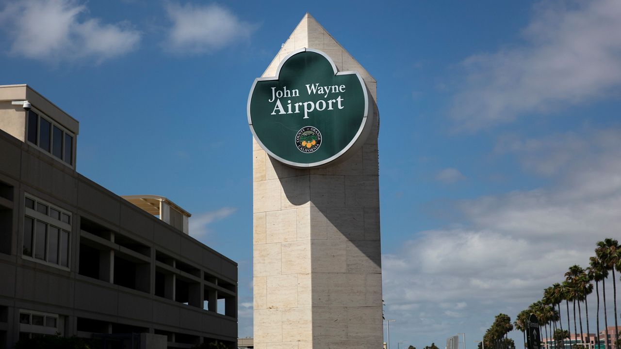 A John Wayne Airport sign stands next to a parking structure at John Wayne Airport in Santa Ana, Calif., Monday, June 29, 2020. In the latest move to change place names in light of U.S. racial history, leaders of Orange County's Democratic Party are pushing to drop film legend Wayne's name, statue and other likenesses from the county's airport because of his racist and bigoted comments. (AP Photo/Jae C. Hong)