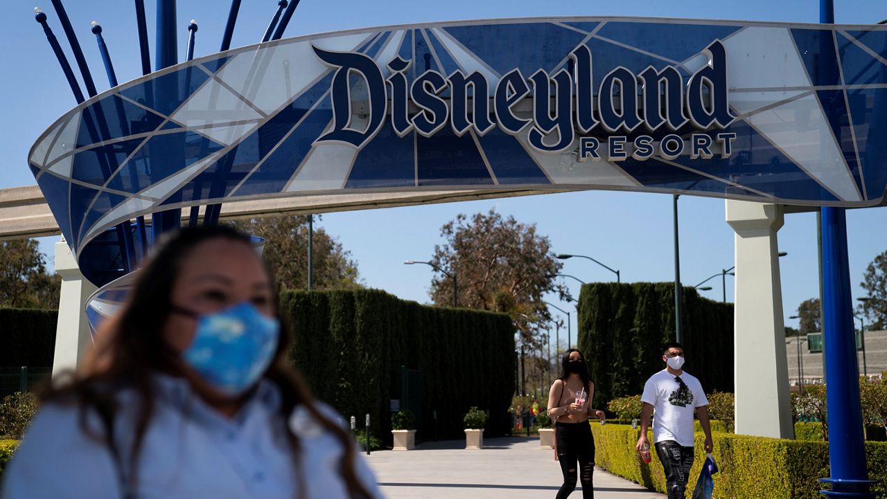 In this March 9, 2021, file photo, a woman with a mask waits to cross the street outside Disneyland Resort in Anaheim. The chief executive of the Walt Disney Company, Bob Chapek, said that Disneyland Resort will likely reopen by late April. (AP Photo/Jae C. Hong)