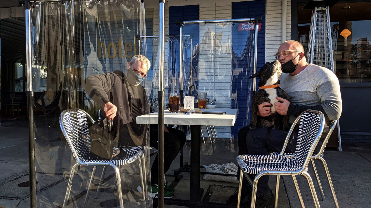 John Davidson, left, and Chris Charles, with his dog Clyde, sit outdoors at the Swingers Diner on Beverly Boulevard Thursday in Los Angeles.  (AP Photo/Damian Dovarganes)