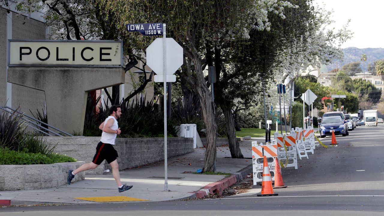 In this February 8, 2013, file photo, a man jogs on the street in front of the West Los Angeles police station that has yellow tape prohibiting the parking of cars. (AP Photo/Reed Saxon)