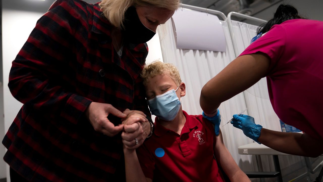 Heather Haworth, left, holds the hand of her 12-year-old son Jeremy as he receives the first dose of the Pfizer COVID-19 vaccine Thursday from medical assistant Gloria Urgell at Providence Edwards Lifesciences vaccination site in Santa Ana. (AP Photo/Jae C. Hong)