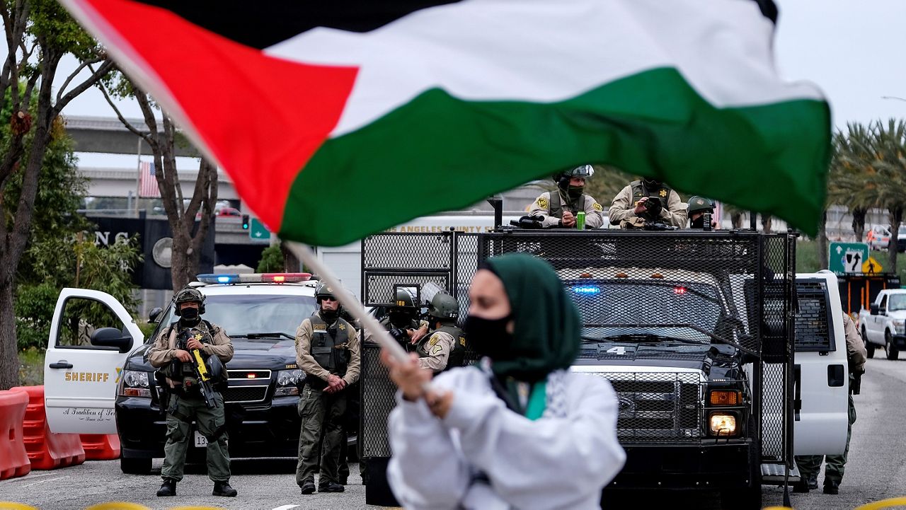 A demonstrator waves the flag of Palestine as police officers guard outside the Federal Building during a protest Saturday against Israel and in support of Palestinians in the Westwood section of Los Angeles. (AP Photo/Ringo H.W. Chiu)