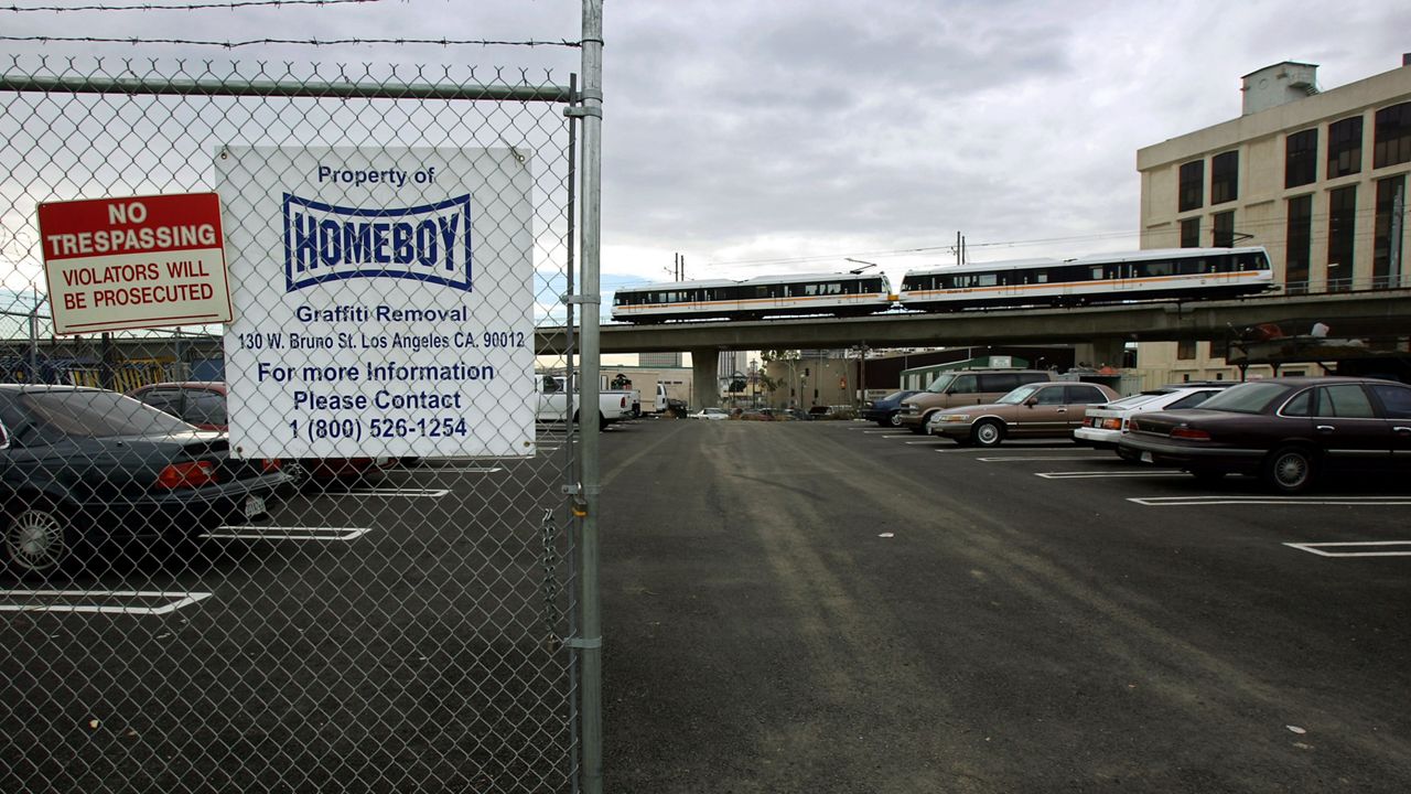 In this Nov. 23, 2014, file photo, a sign marks the future site of the home of Homeboy Industries as a Metro Gold Line train rolls by near Chinatown in downtown Los Angeles. (AP Photo/Kevork Djansezian)