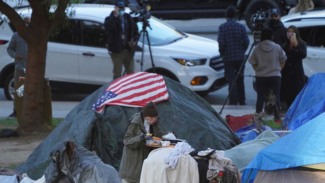 In this March 24, 2021, file photo, a woman eats at her tent at the Echo Park homeless encampment at Echo Park Lake in Los Angeles. (AP Photo/Damian Dovarganes, File)