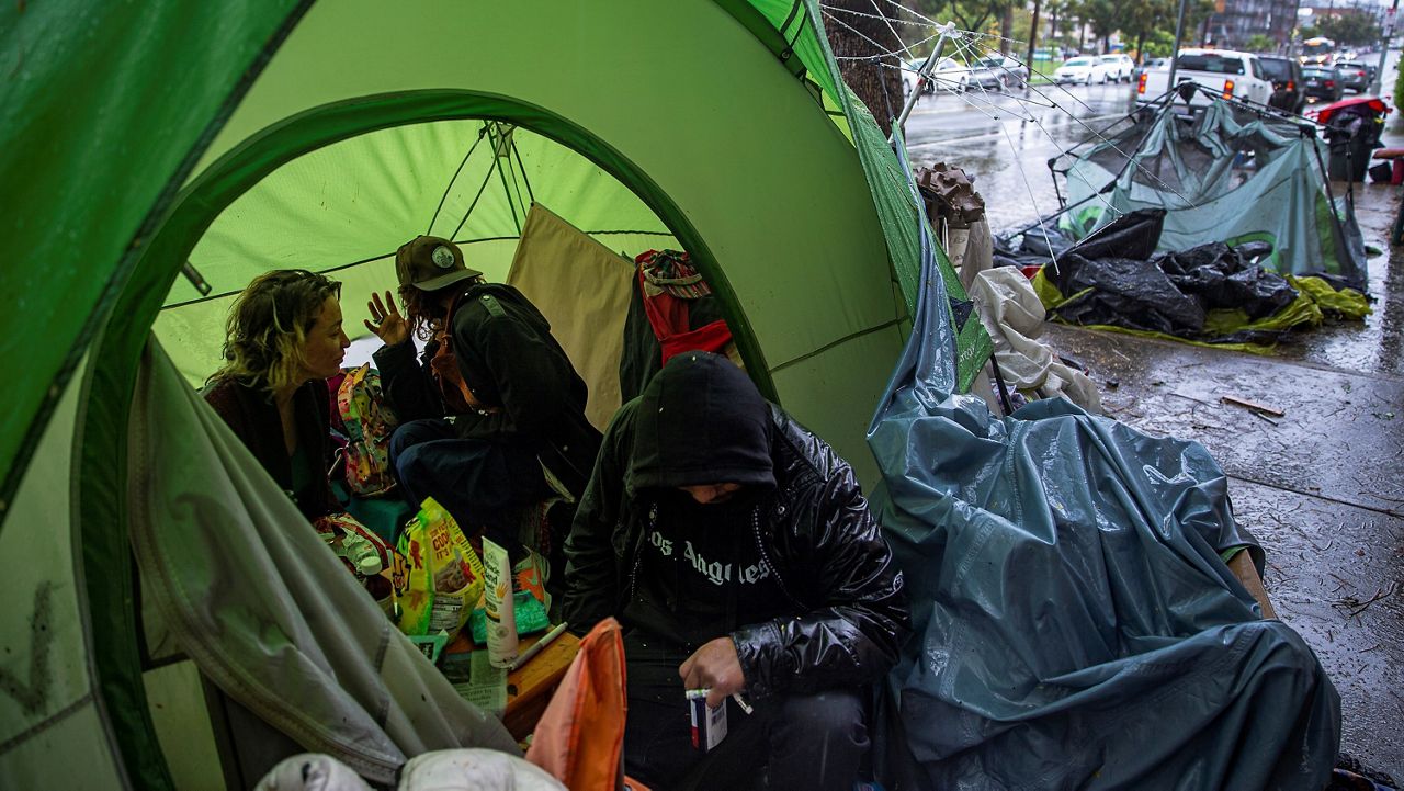 People try to stay warm as they face the elements inside a homeless encampment flooded under a rainstorm across Echo Park Lake in Los Angeles on March 12, 2020. (AP Photo/Damian Dovarganes)