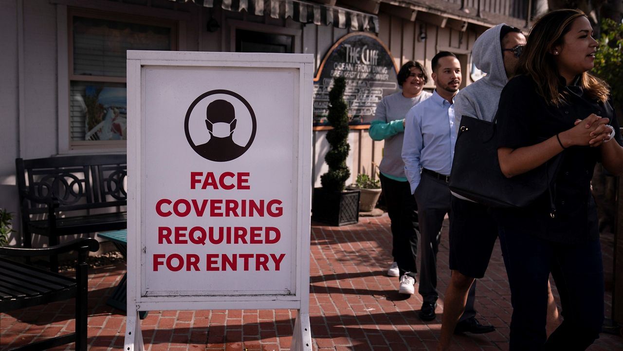 In this May 17, 2021, file photo, people walk past a sign requesting customers to wear masks in Laguna Beach, Calif. (AP Photo/Jae C. Hong)