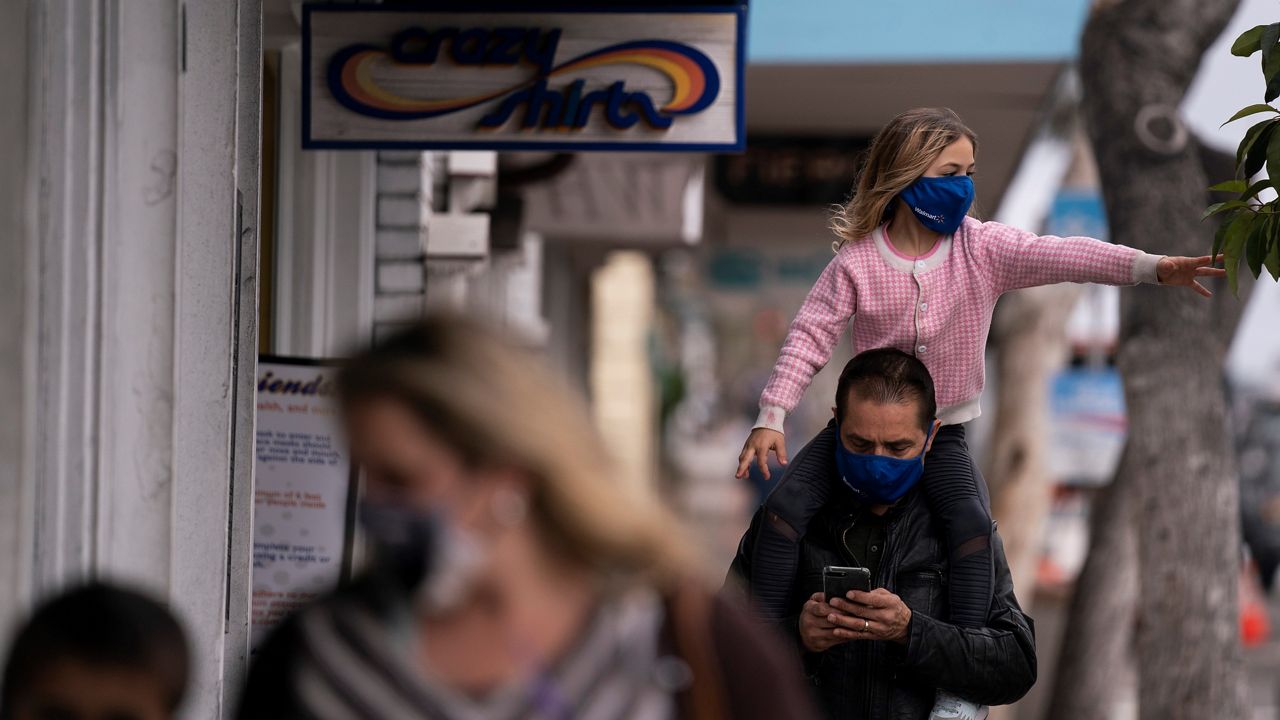 Bijan Parsi looks at his phone while carrying his daughter Ava, 6, on his shoulders in Laguna Beach, Calif. on May 17, 2021. (AP Photo/Jae C. Hong)