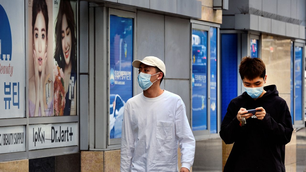 In this Feb. 28, 2020, file photo, two friends, both wearing protective masks, walk along a street in the Koreatown section of Los Angeles. (AP Photo/Richard Vogel)