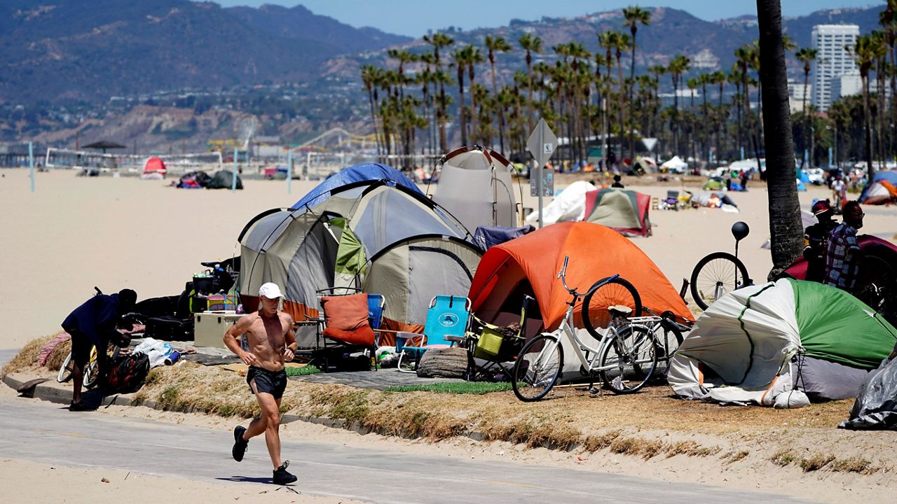 In this June 8, 2021, file photo, a jogger walks past a homeless encampment in the Venice Beach section of Los Angeles. (AP Photo/Marcio Jose Sanchez)