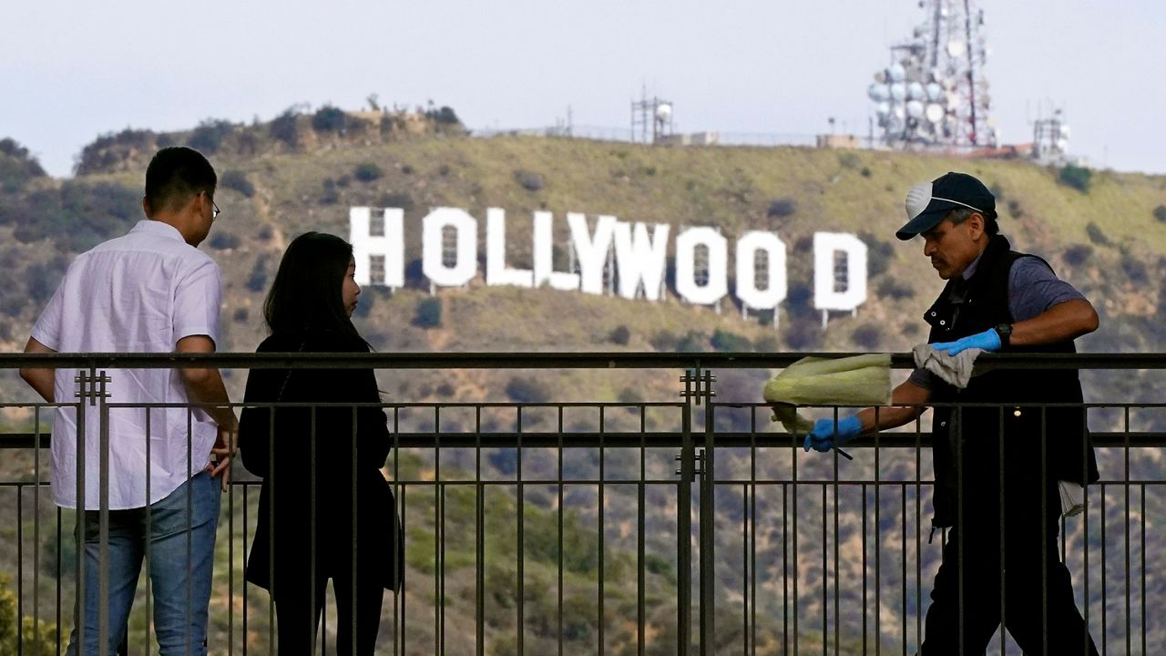 Pedestrians look at the Hollywood sign as a worker cleans the rails at Hollywood & Highland in the Hollywood section of Los Angeles on March 18, 2020. (AP Photo/Mark J. Terrill)