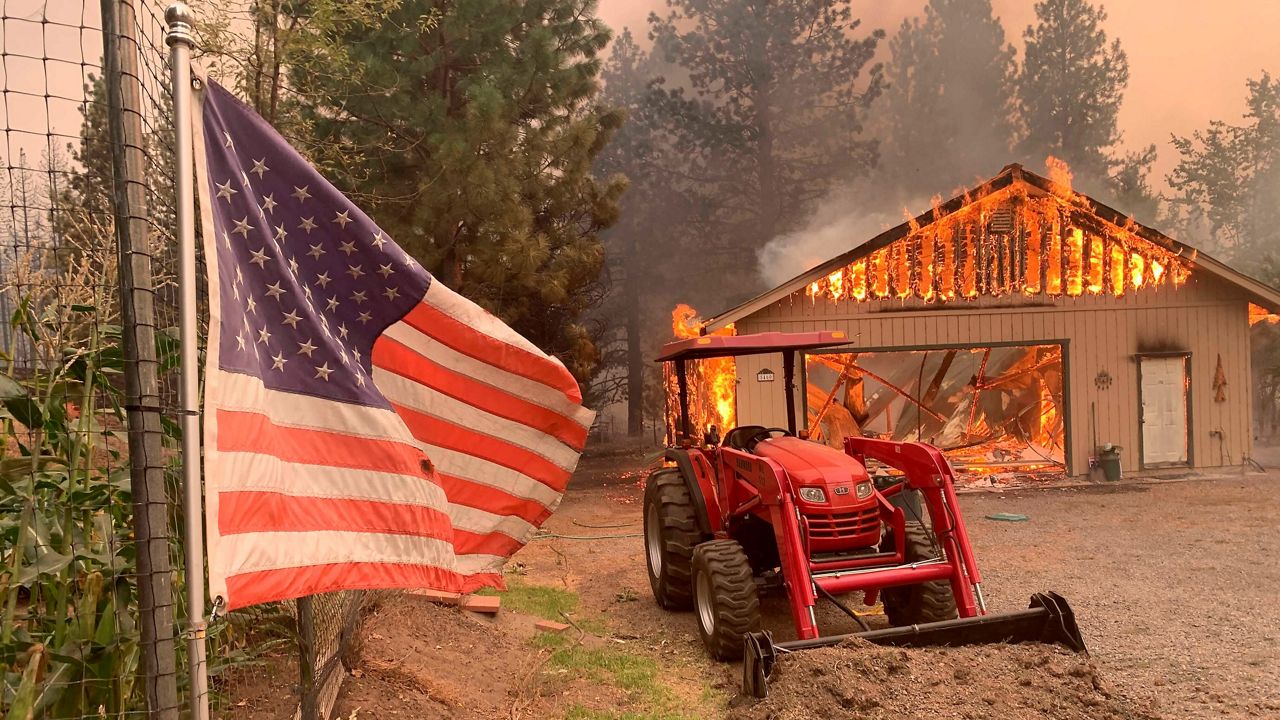 A red tractor is left behind as a home burns Friday outside of Taylorsville in Plumas County, Calif., that was impacted by the Dixie Fire. (AP Photo/Eugene Garcia)