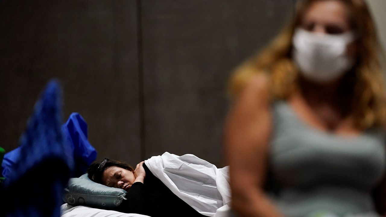 In this Aug. 11, 2020, file photo, a woman sleeps as another sits on her cot in a homeless shelter inside the San Diego Convention Center in San Diego. (AP Photo/Gregory Bull)