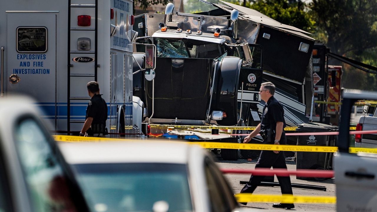 In this July 1, 2021, file photo, police officers walk past the remains of an armored Los Angeles Police Department tractor-trailer after illegal fireworks seized at a South Los Angeles home exploded. (AP Photo/Damian Dovarganes)