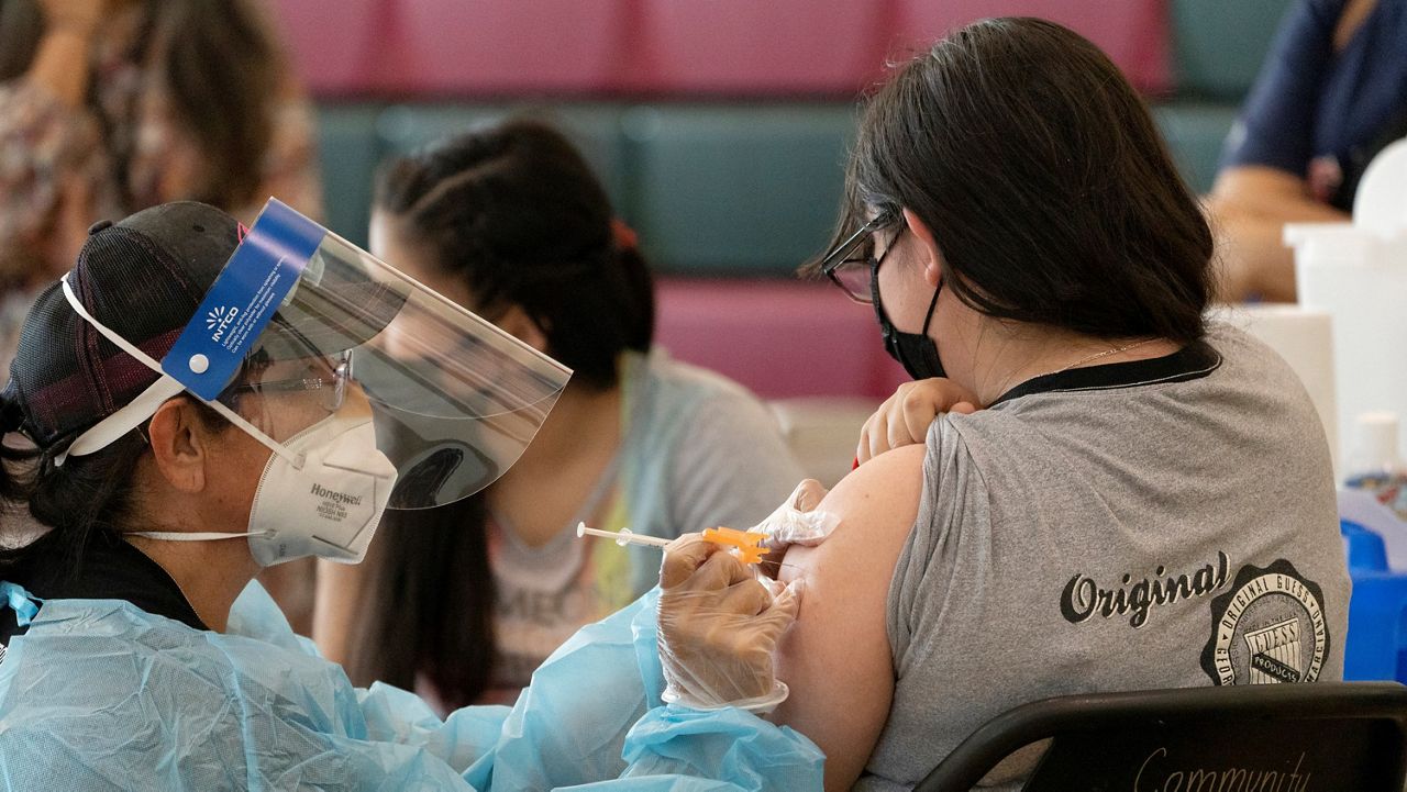 Sisters Guadalupe Flores, 15, right, and Estela Flores, 13, left, from East Los Angeles, get vaccinated with the Pfizer's COVID-19 vaccine by licensed vocational nurse Rita Orozco, far left, at the Esteban E. Torres High School in Los Angeles on May 27, 2021. (AP Photo/Damian Dovarganes)