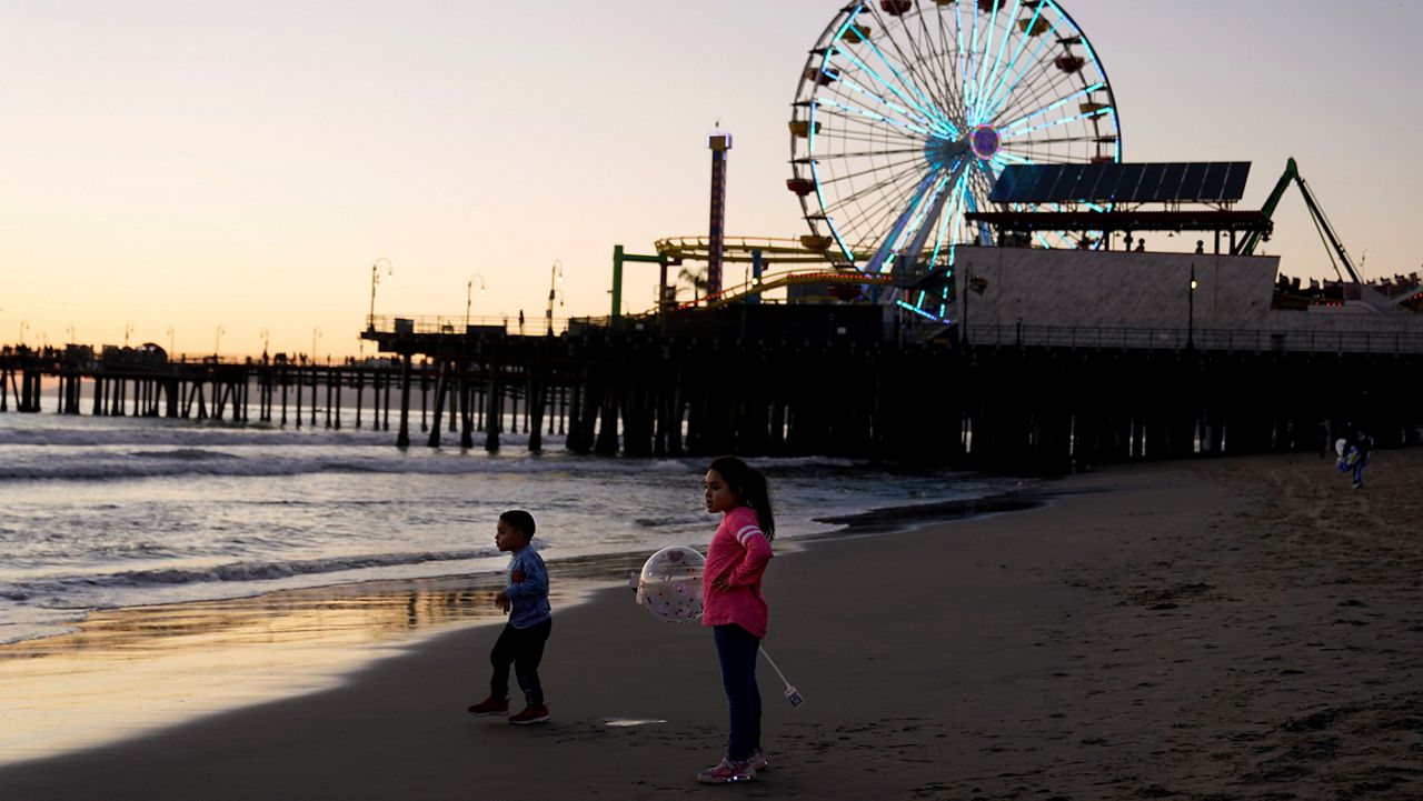 In this Feb. 19, 2021, file photo, young visitors watch the sunset near the pier in Santa Monica, Calif. (AP Photo/Marcio Jose Sanchez)