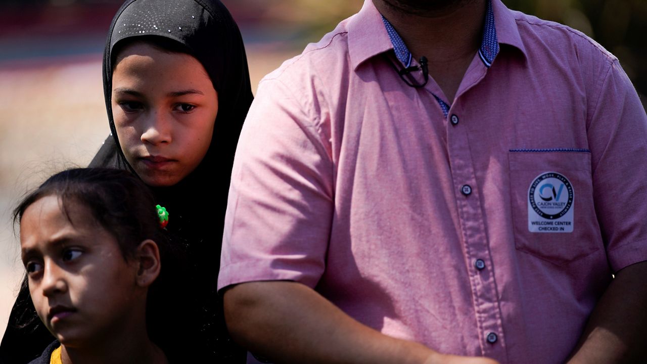 Palwasha Faizi, 10, left, stands behind her sister, Parwana Faizi, 7, and alongside her father, Mohammad Faizi, during a news conference Thursday in El Cajon, Calif. In August, the family visited relatives in Afghanistan and were forced to escape as the Taliban seized power. (AP Photo/Gregory Bull)