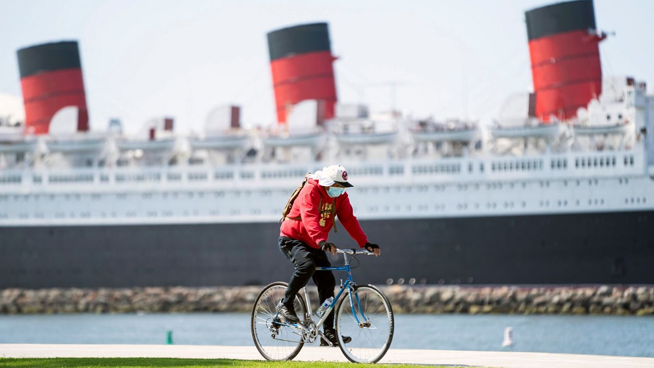In this May 11, 2020, file photo, a bicyclist wearing a face mask rides past The Queen Mary hotel in Long Beach, Calif. (AP Photo/Ashley Landis)