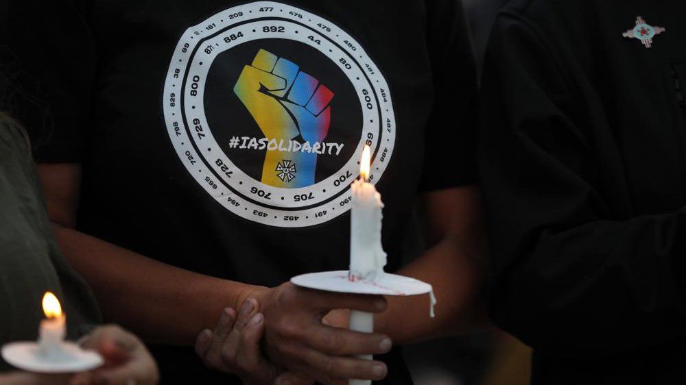Movie industry worker Hailey Josselyn, wearing a T-shirt of the International Alliance of Theatrical Stage Employees, or IATSA, holds a candle during Saturday's vigil to honor cinematographer Halyna Hutchins in Albuquerque, N.M. (AP Photo/Andres Leighton)
