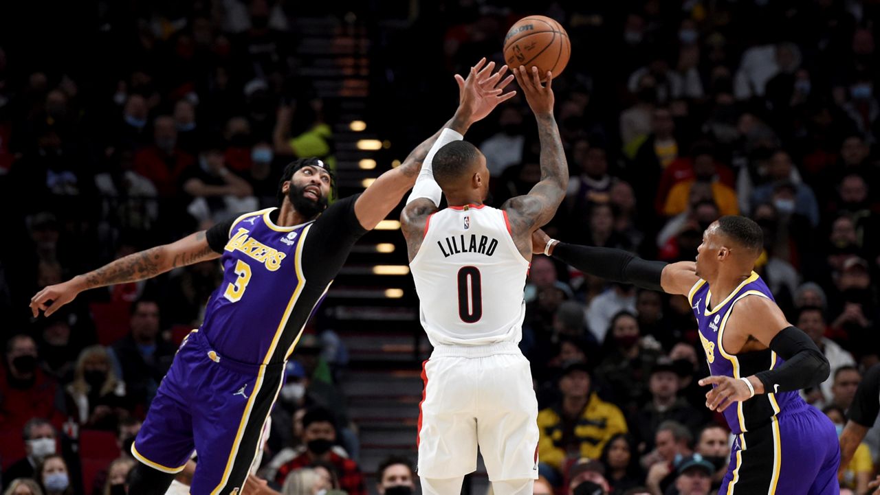 Portland Trail Blazers guard Damian Lillard, center, hits a 3-point shot from between Los Angeles Lakers Anthony Davis, left, and guard Russell Westbrook during the first half of an NBA basketball game Saturday in Portland, Ore. (AP Photo/Steve Dykes)