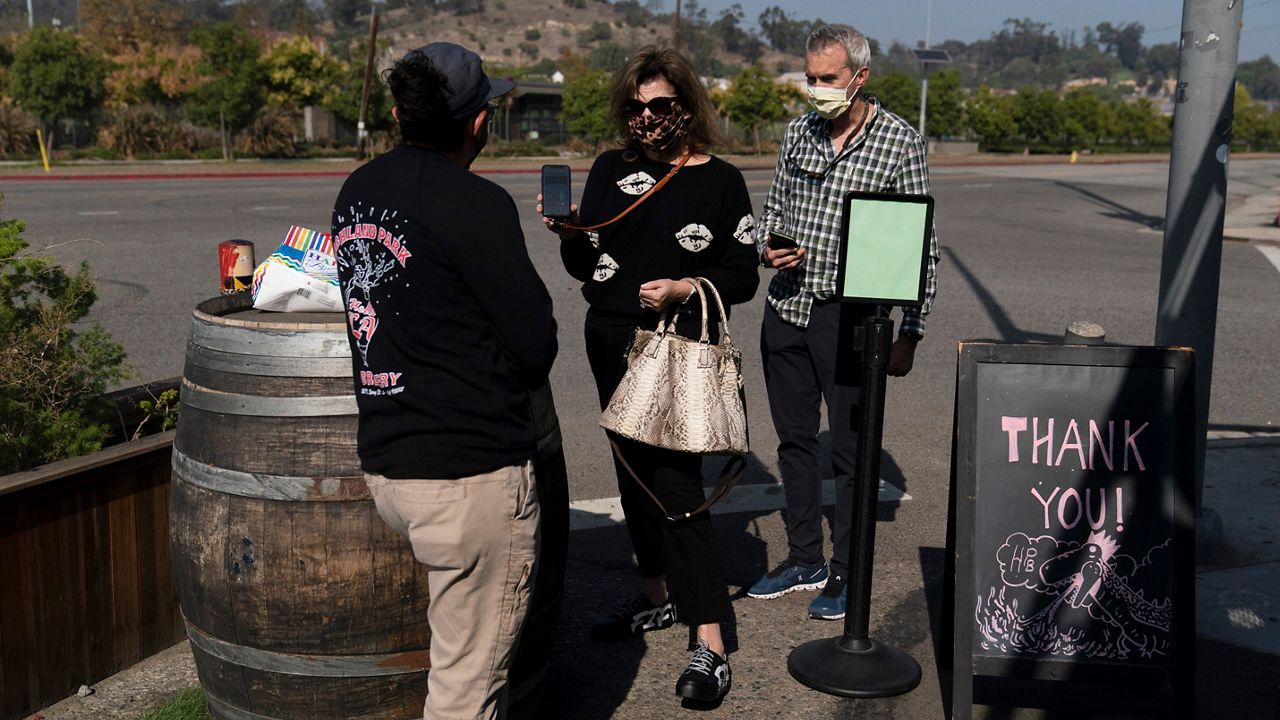 In this Nov. 8, 2021, file photo, Marta McKay, center, and her husband, Bob, show a restaurant worker their proof of COVID-19 vaccination as they enter Highland Park Brewery in Los Angeles. (AP Photo/Jae C. Hong)