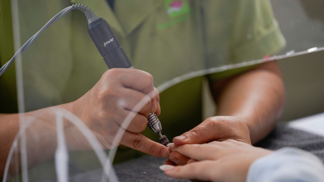 In this July 22, 2020, file photo, a beauty salon employee works on a customer's nails from under a plexiglass shield outside Pampered Hands nail salon in Los Angeles. (AP Photo/Ashley Landis)