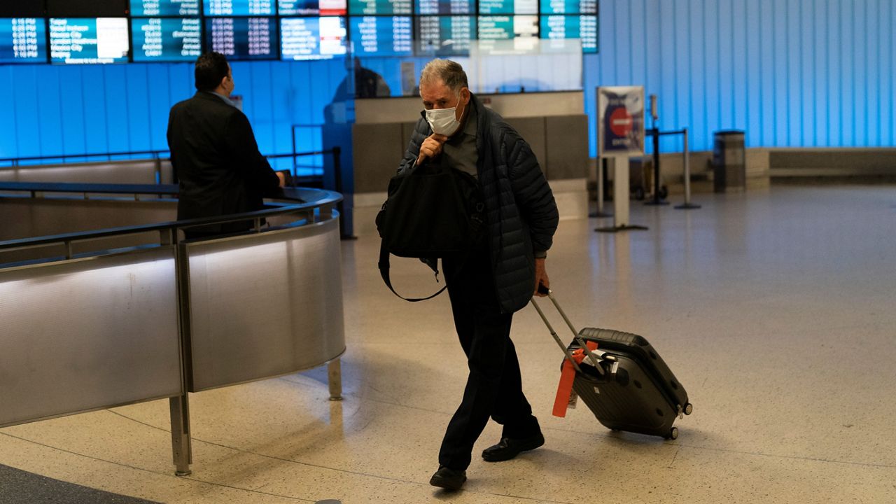 In this Nov. 30, 2021, file photo, a traveler adjusts his face mask as he walks through the arrivals area at the Los Angeles International Airport in Los Angeles. (AP Photo/Jae C. Hong)