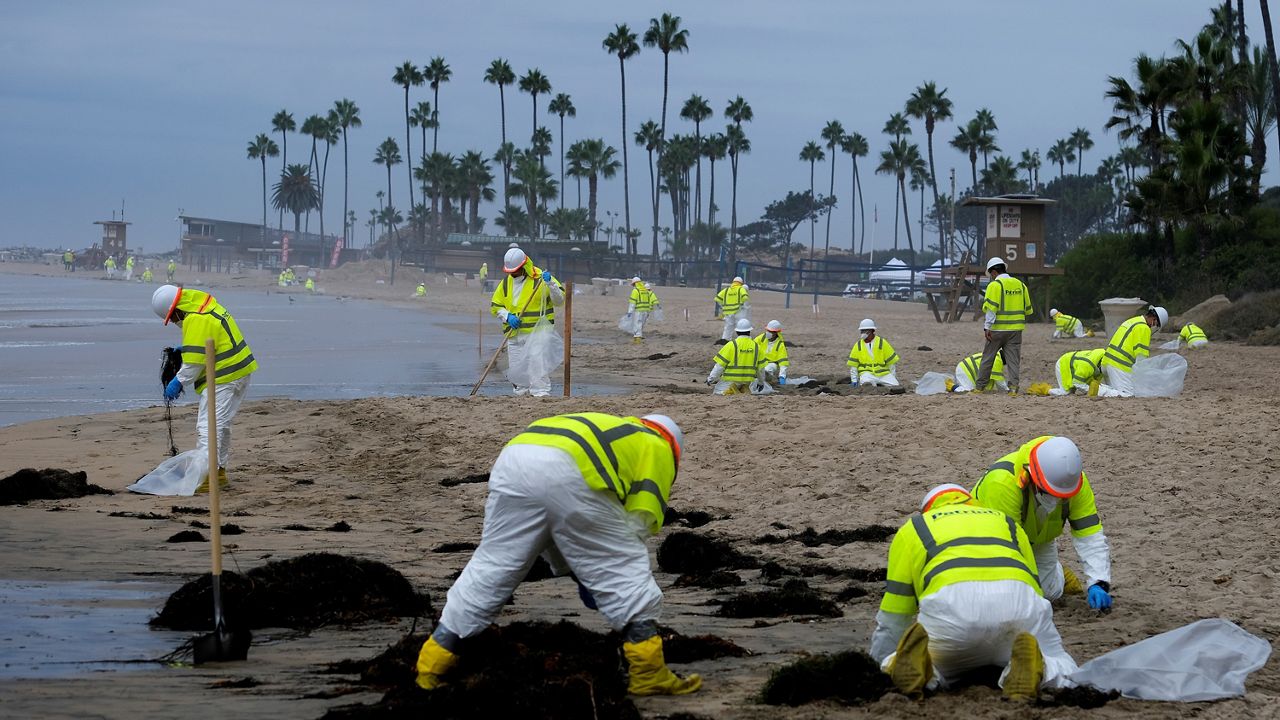 In this Oct. 7, 2021, file photo, workers in protective suits clean the contaminated beach in Corona Del Mar after an oil spill off the Southern California coast. (AP Photo/Ringo H.W. Chiu)