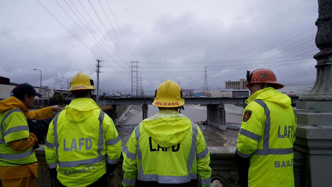 Los Angeles firefighters wait for the water level to fall while looking down at a submerged vehicle wedged against a bridge pillar in the surging Los Angeles River Tuesday in Los Angeles. No victims, if any, were immediately located. (AP Photo/Damian Dovarganes)