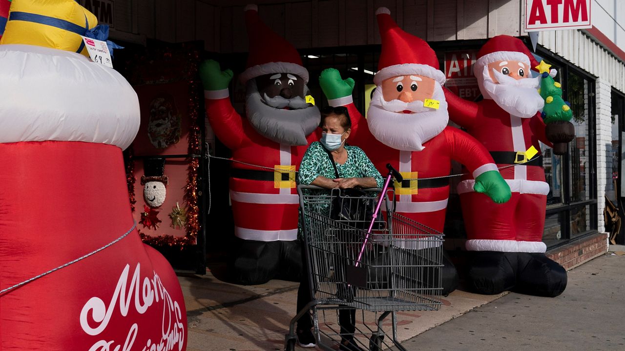 A shopper wearing a face mask pushes an empty cart past inflatable Santa Clauses as she leaves a discount store Monday in Inglewood, Calif. Omicron has raced ahead of other variants and is now the dominant version of the coronavirus in the U.S., accounting for 73% of new infections last week, federal health officials said Monday. (AP Photo/Jae C. Hong)