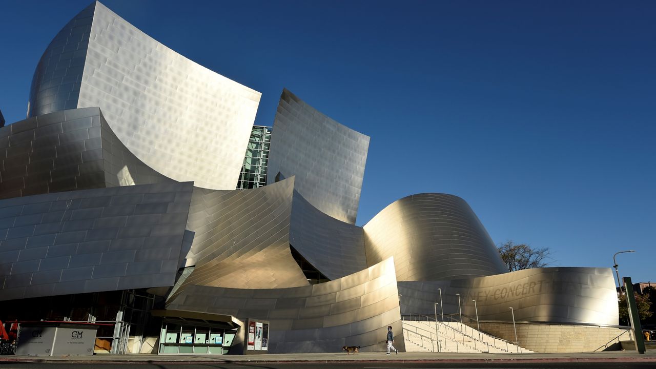 In this April 25, 2020, file photo, a woman walks her dog past the Walt Disney Concert Hall on deserted Grand Avenue as stay-at-home orders continue due to the coronavirus pandemic in Los Angeles. (AP Photo/Chris Pizzello)