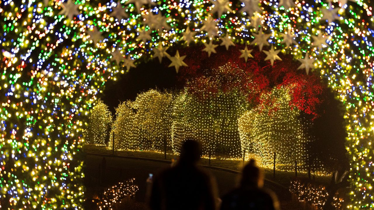 In this Dec. 10, 2021, file photo, visitors walk through a light tunnel at a Holiday Road light show in Calabasas, Calif. The pandemic turned the annual light festival into a drive-thru event last year. (AP Photo/Jae C. Hong)