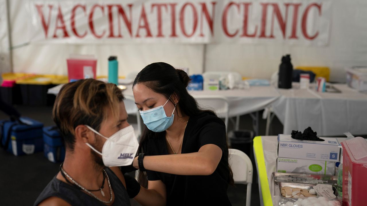 In this Aug. 28, 2021, file photo, registered nurse Noleen Nobleza, center, inoculates Julio Quinones with a COVID-19 vaccine at a clinic set up in the parking lot of CalOptima in Orange, Calif. (AP Photo/Jae C. Hong)