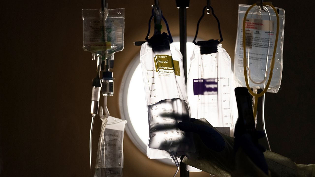 In this Dec. 13, 2021, file photo, nurse manager Edgar Ramirez checks on IV fluids while talking to a COVID-19 patient at Providence Holy Cross Medical Center in Los Angeles. (AP Photo/Jae C. Hong)