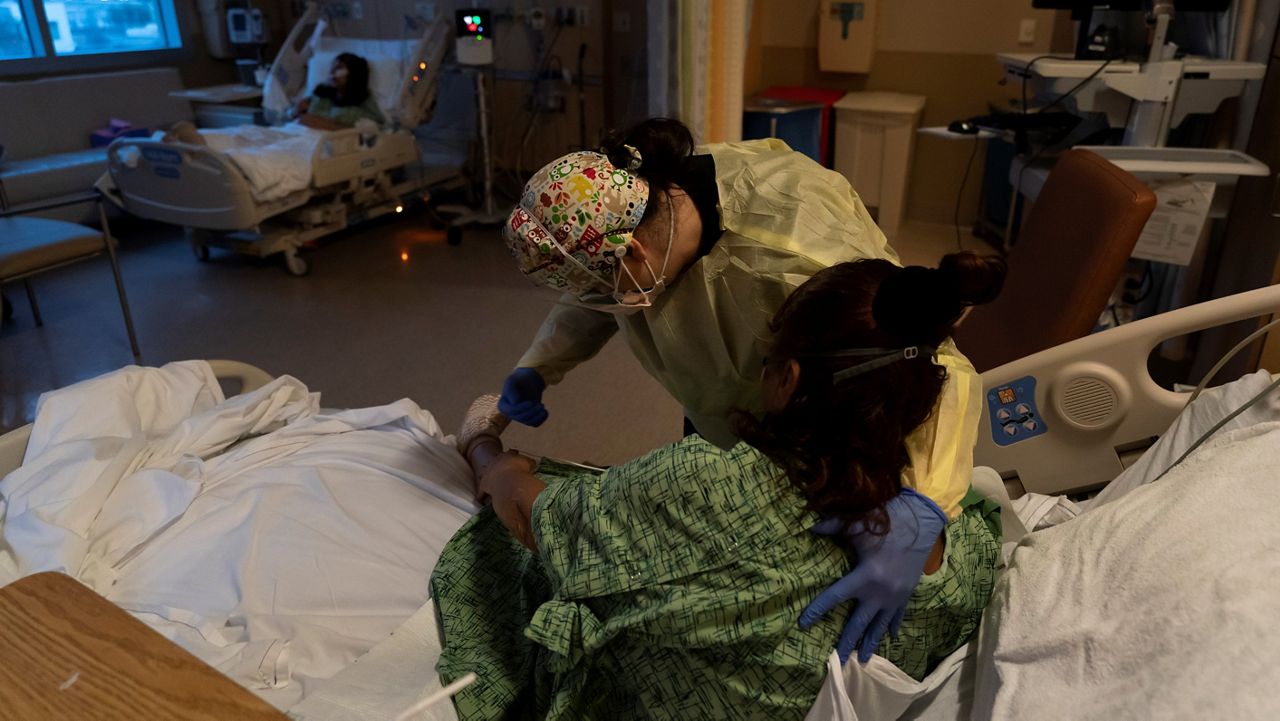 In this Dec. 13, 2021, file photo, registered nurse Nvard Termendzhyan helps Linda Calderon, a 71-year-old COVID-19 patient, sit up at Providence Holy Cross Medical Center in Los Angeles. (AP Photo/Jae C. Hong)
