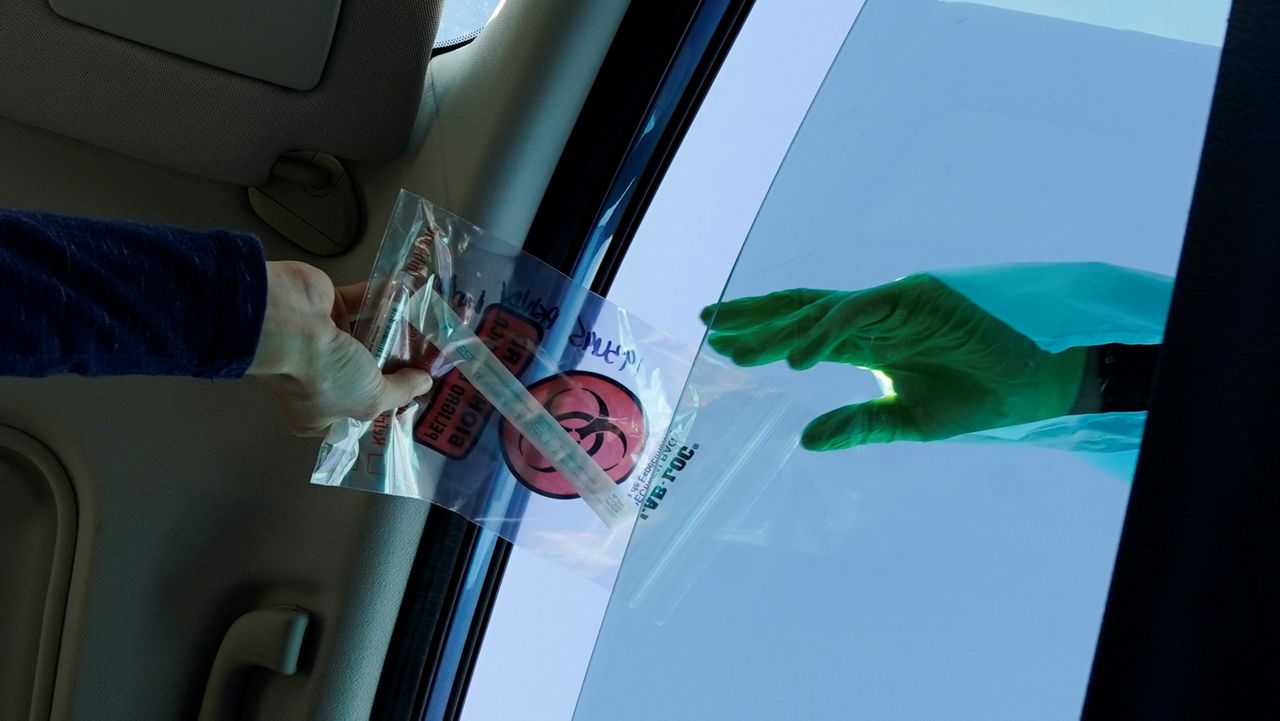 In this Dec. 1, 2020, file photo, a COVID-19 test is handed through the vehicle window at a mobile testing site in Long Beach, Calif. (AP Photo/Ashley Landis)