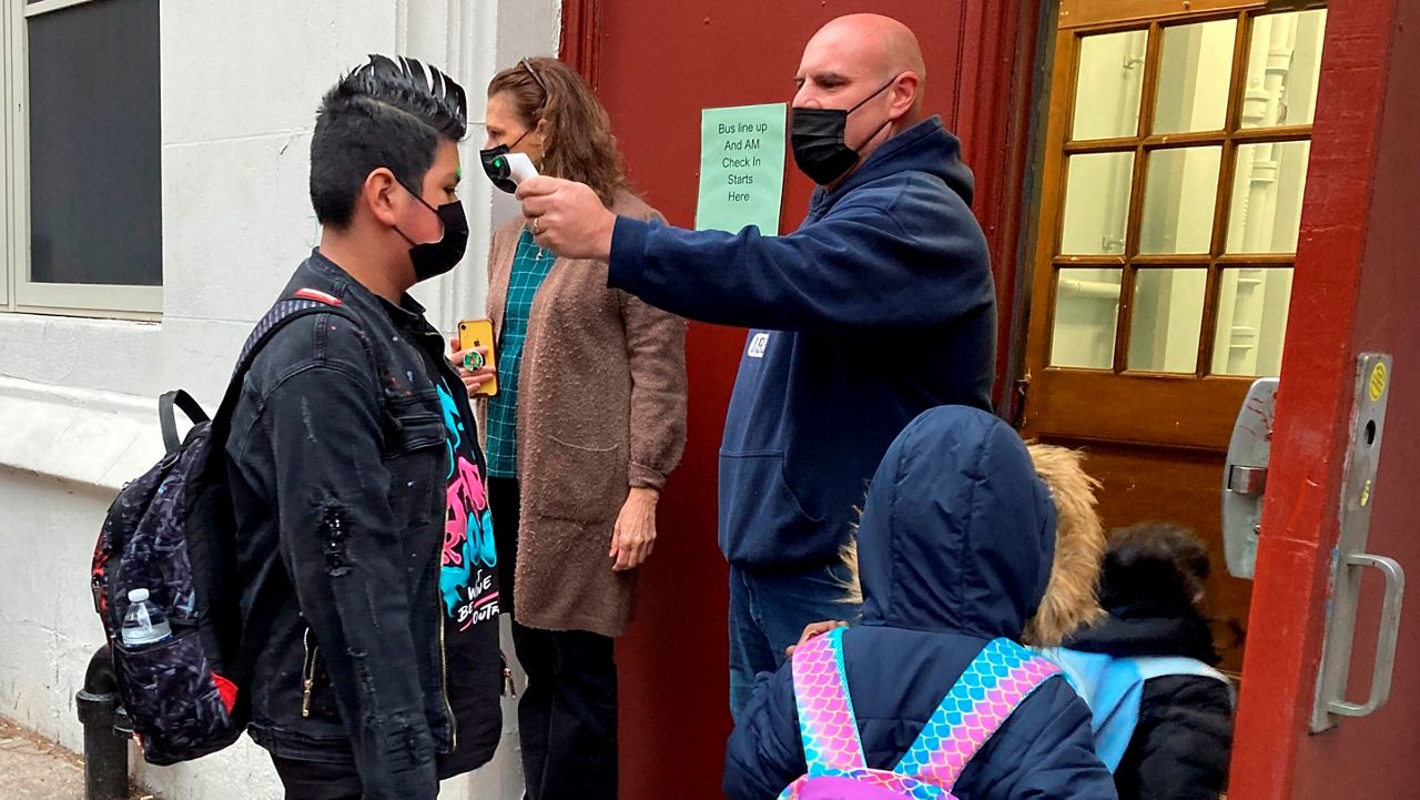 John Marro, the dean of students at P.S. 347, The American Sign Language and English Lower School, in New York, takes students' temperatures as they arrive on the first day after the holiday break, Monday, Jan. 3, 2022. New York City schools reopened Monday after the holiday break despite a surge in coronavirus infections. (AP Photo/Jennifer Peltz)