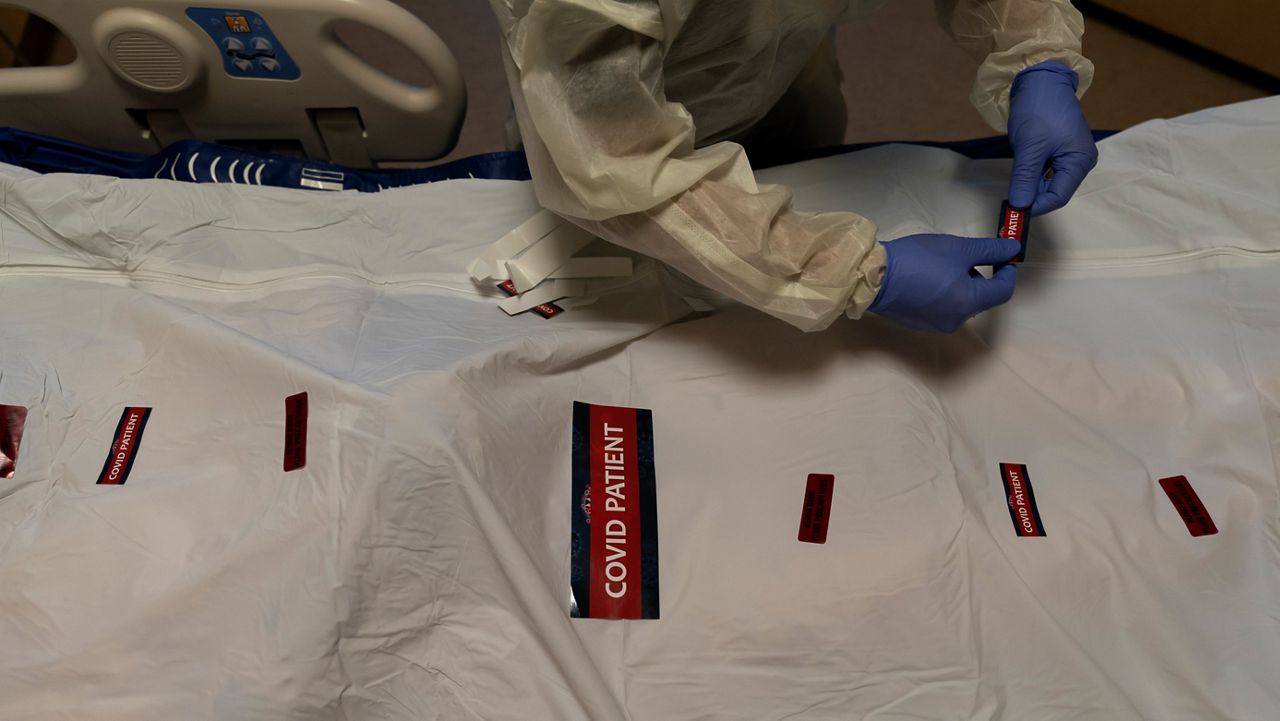 In this Dec. 14, 2021, file photo, registered nurse Bryan Hofilena attaches "COVID Patient" stickers on a body bag of a patient who died of coronavirus at Providence Holy Cross Medical Center in Los Angeles. (AP Photo/Jae C. Hong)