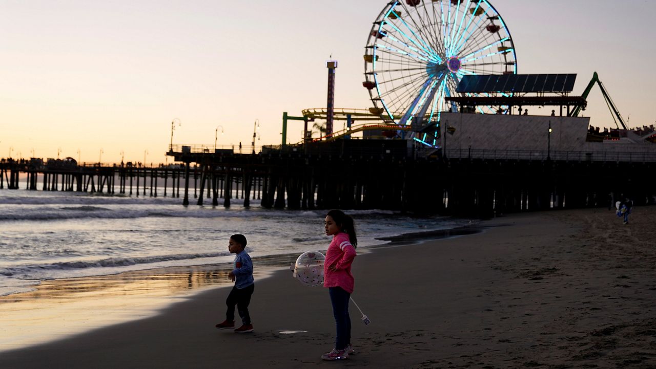 In this Feb. 19, 2021, file photo, young visitors watch the sunset near the pier in Santa Monica, Calif. (AP Photo/Marcio Jose Sanchez)