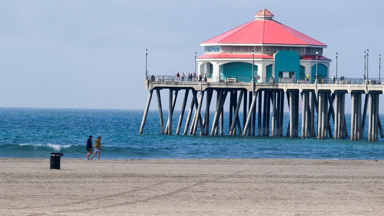 People walk along a beach near the pier in Huntington Beach, Calif., Monday, Oct. 11, 2021. (AP Photo/Ringo H.W. Chiu)