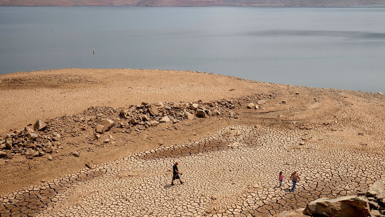 In this Aug. 22, 2021, file photo, a family walks over cracked mud near Lake Oroville’s shore as water levels remain low due to continuing drought conditions in Oroville, Calif. (AP Photo/Ethan Swope)