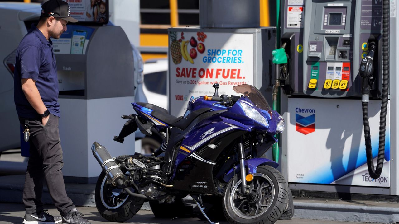 A motorcycle rider fixes his bike at a gas station on March 7, 2022, in Los Angeles. (AP Photo/Damian Dovarganes)