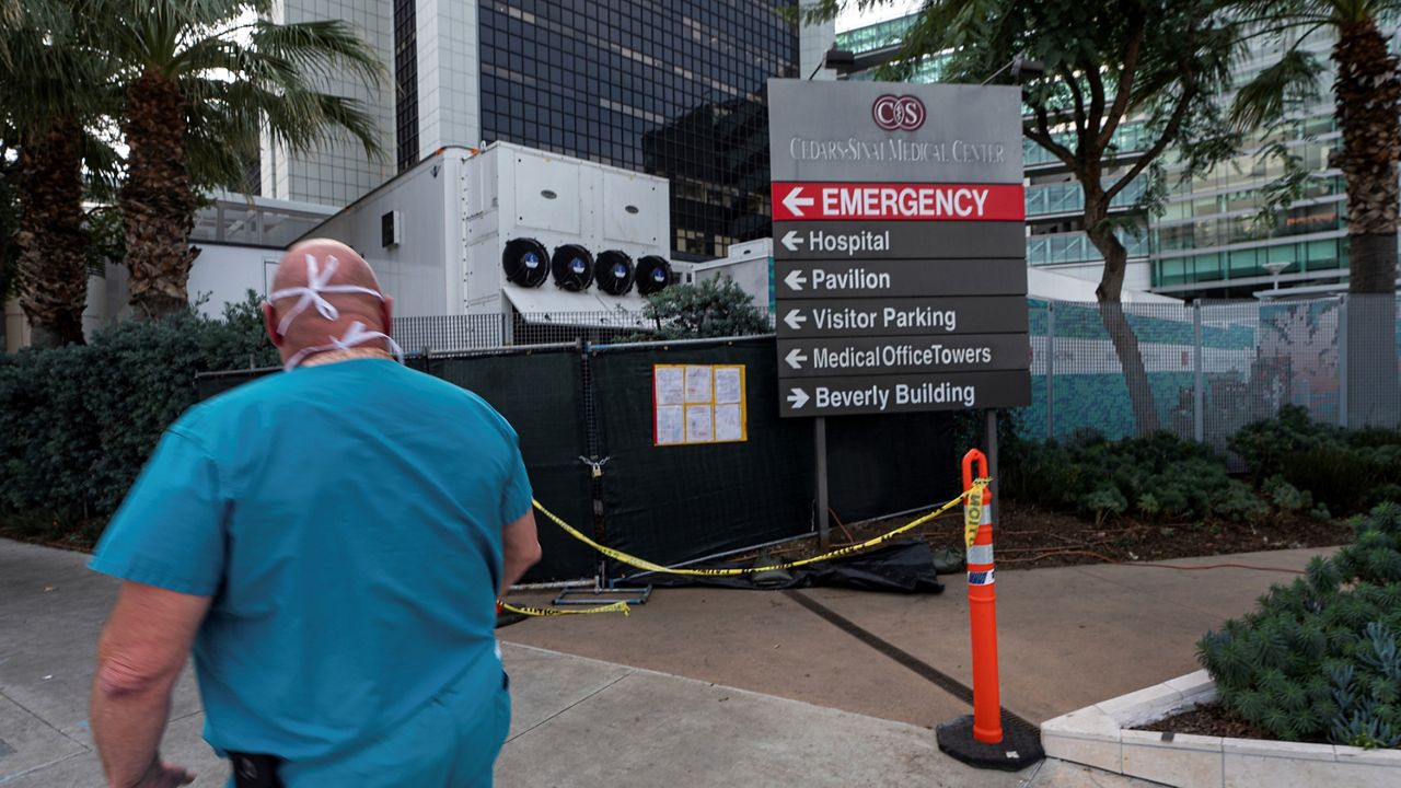 In this Jan. 7, 2021, file photo, a medical worker walks past a refrigerated trailer parked outside the Cedars-Sinai Medical Center in Los Angeles. (AP Photo/Damian Dovarganes)