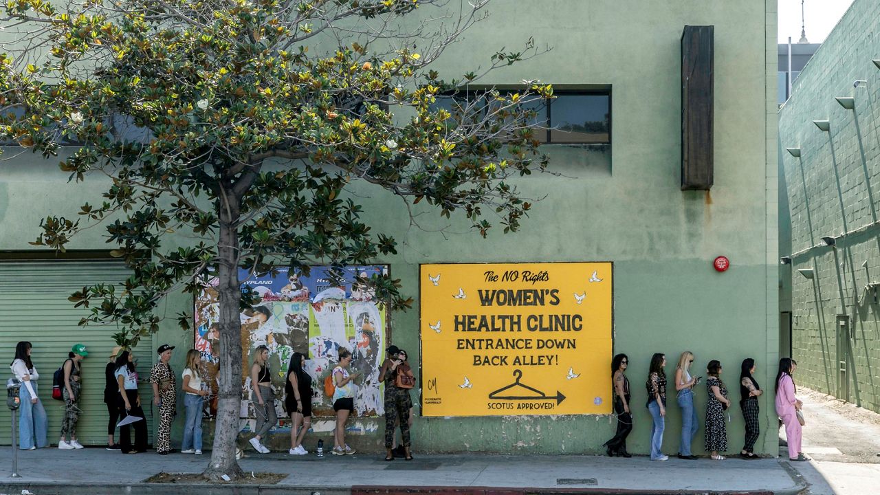 In this photo provided by Elizabeth Daniels, women line up next to a sign advertising back-alley abortions on June 28, 2022, by street artist Corie Mattie on a heavily trafficked stretch of Highland Avenue in the Hollywood district of Los Angeles. (Elizabeth Daniels via AP)