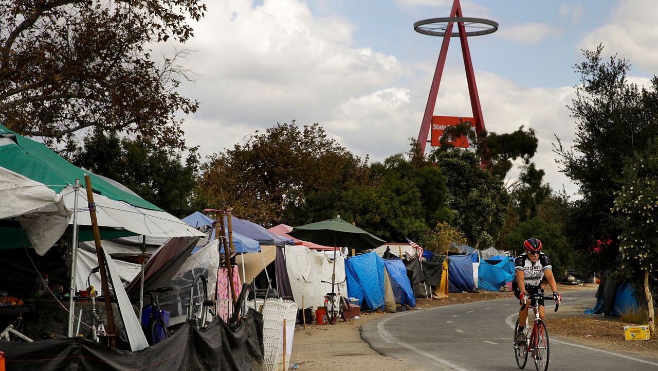 A cyclist passes the row of tents and tarps along the Santa Ana riverbed near Angel Stadium on Sept. 14, 2017, in Anaheim, Calif. (AP Photo/Jae C. Hong)