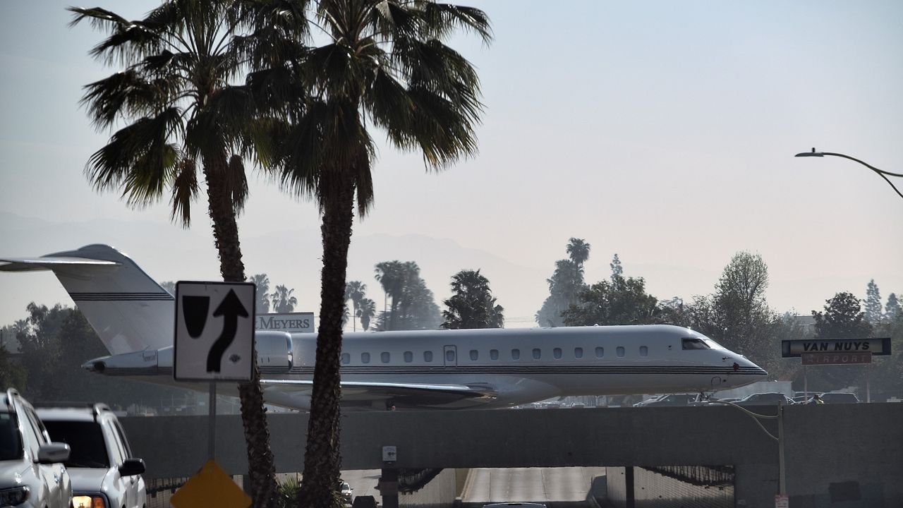 A private jet aircraft taxiing on a runway as city traffic passes underneath a bridge at the Van Nuys Airport in Los Angeles on April 10, 2021. (AP Photo/Richard Vogel)