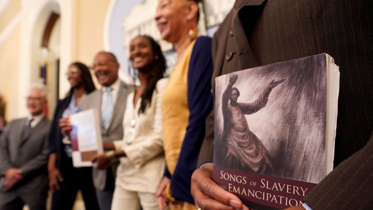 Dr. Amos C. Brown Jr., vice chair for the California Reparations Task Force, right, holds a copy of the book Songs of Slavery and Emancipation, as he and other members of the task force pose for photos on June 16, 2022, at the Capitol in Sacramento, Calif. (AP Photo/Rich Pedroncelli)