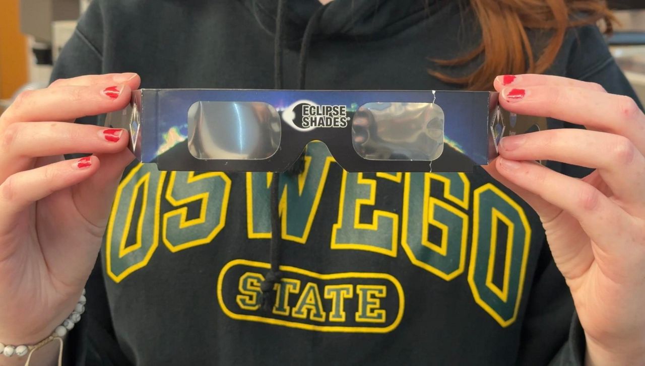 Hands holding eclipse shades, person is wearing a oswego state sweatshirt